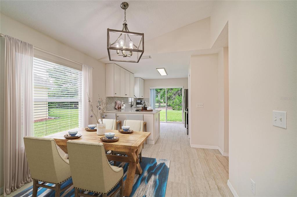 A dining area with a wooden table, pendant light, and tile flooring leads to a kitchen — 6308 ROBIN COVE, BRADENTON, FL