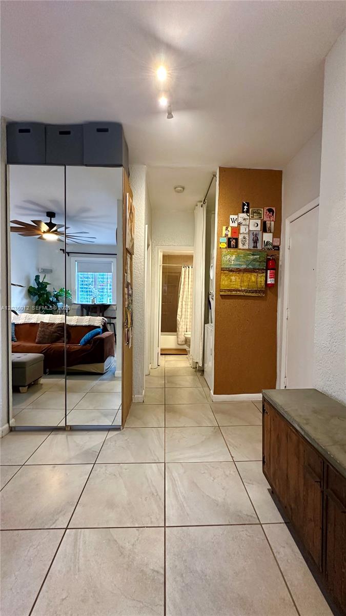 A tiled hallway leads to a bathroom, featuring a mirrored closet and a corkboard wall — 842 Meridian Ave # 1E, Miami Beach FL 33139, MIAMI BEACH, FL