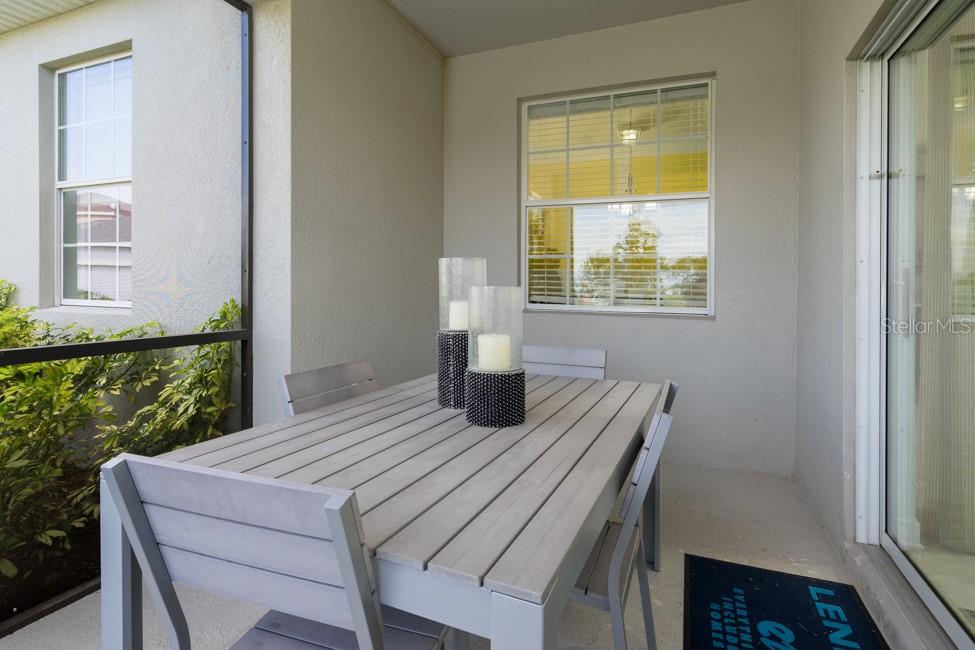 A covered patio features a gray wooden dining set and two pillar candles on the table — 6080 MEDITATION DRIVE, CLERMONT, FL