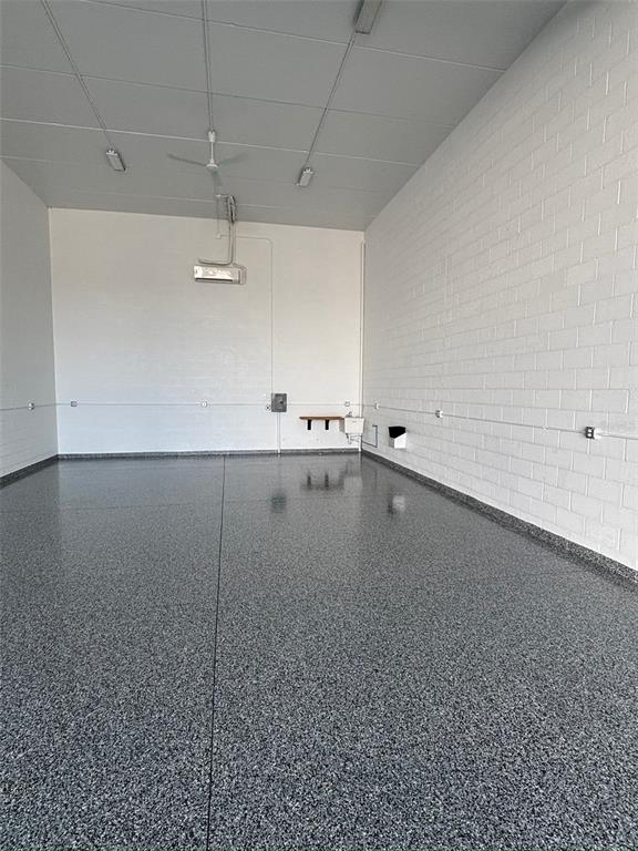A spacious garage with white brick walls, a gray epoxy floor, and a ceiling-mounted projector — 5233 TAYLOR ROAD UNIT B1, PUNTA GORDA, FL