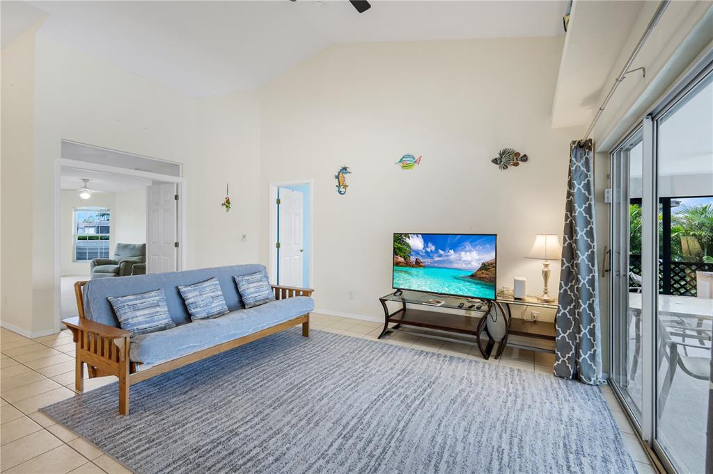 A living room with a futon, television on a stand, and sliding glass doors to outside — 1431 NW 3RD PLACE, CAPE CORAL, FL