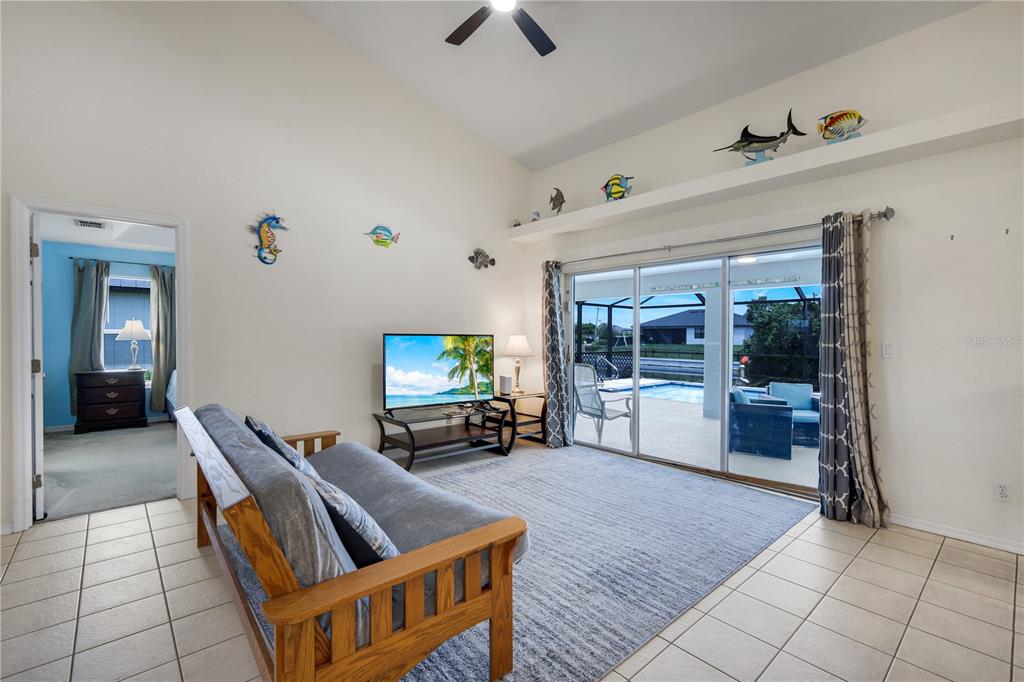 A living room with tile flooring, a futon, a television, and sliding doors to a pool — 1431 NW 3RD PLACE, CAPE CORAL, FL