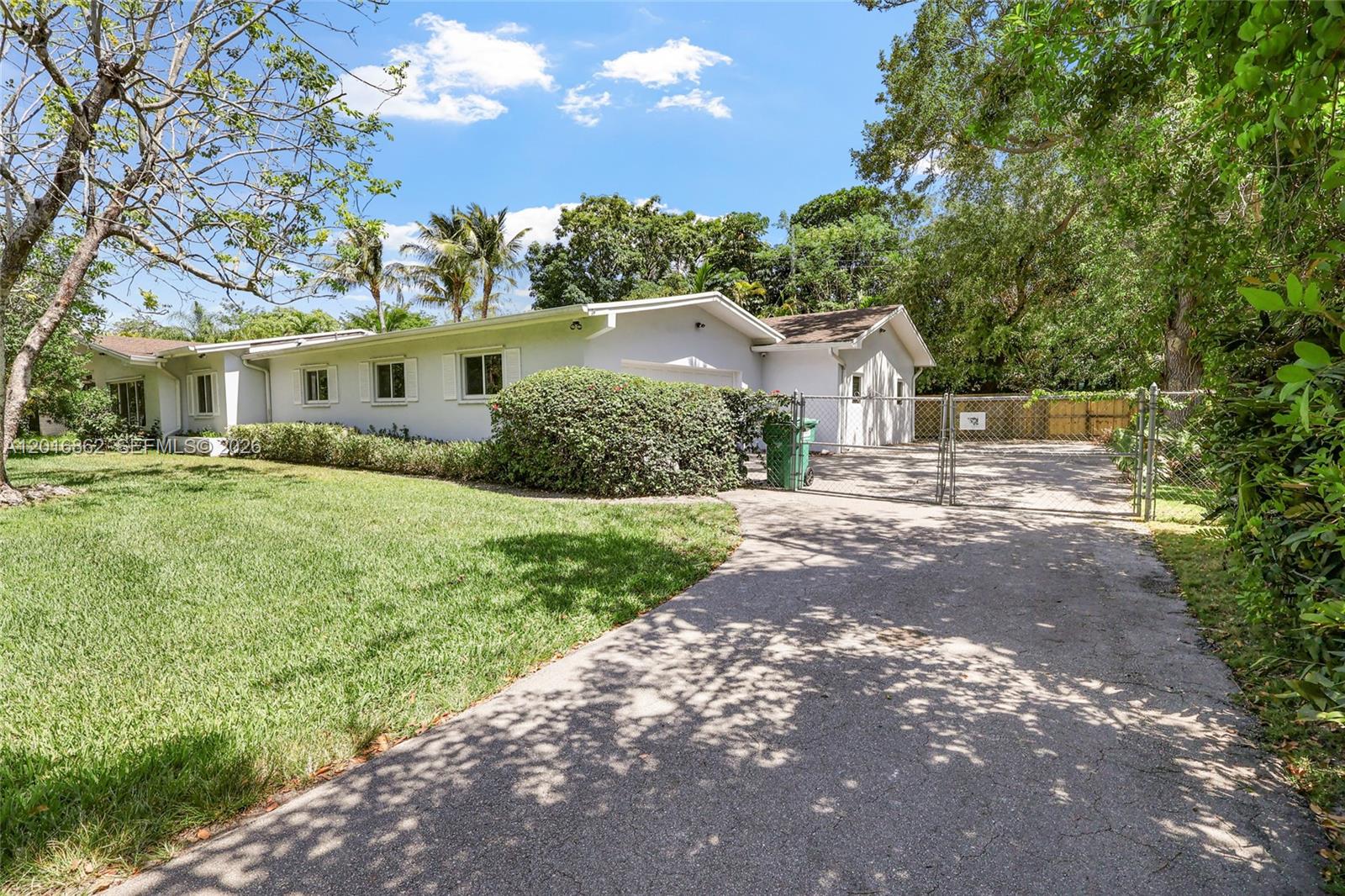 A single-story white house with a paved driveway and a chain-link gate — 7800 SW 132nd St, Pinecrest FL 33156, PINECREST, FL