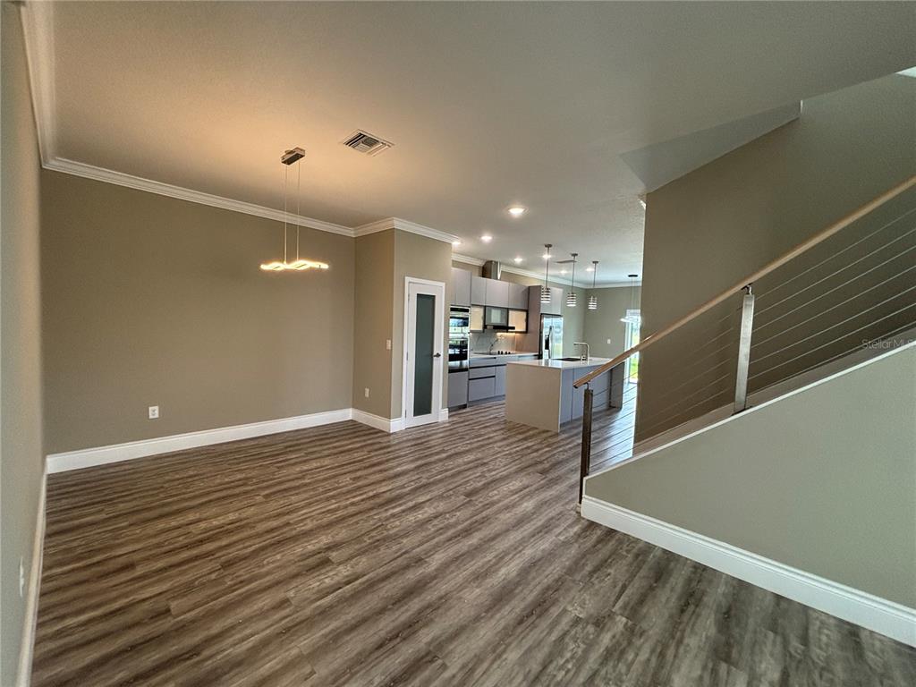 An open-concept living area features wood-look flooring, a modern kitchen, and a staircase with railings — 2049 GREENBRIAR TERRACE, DAVENPORT, FL