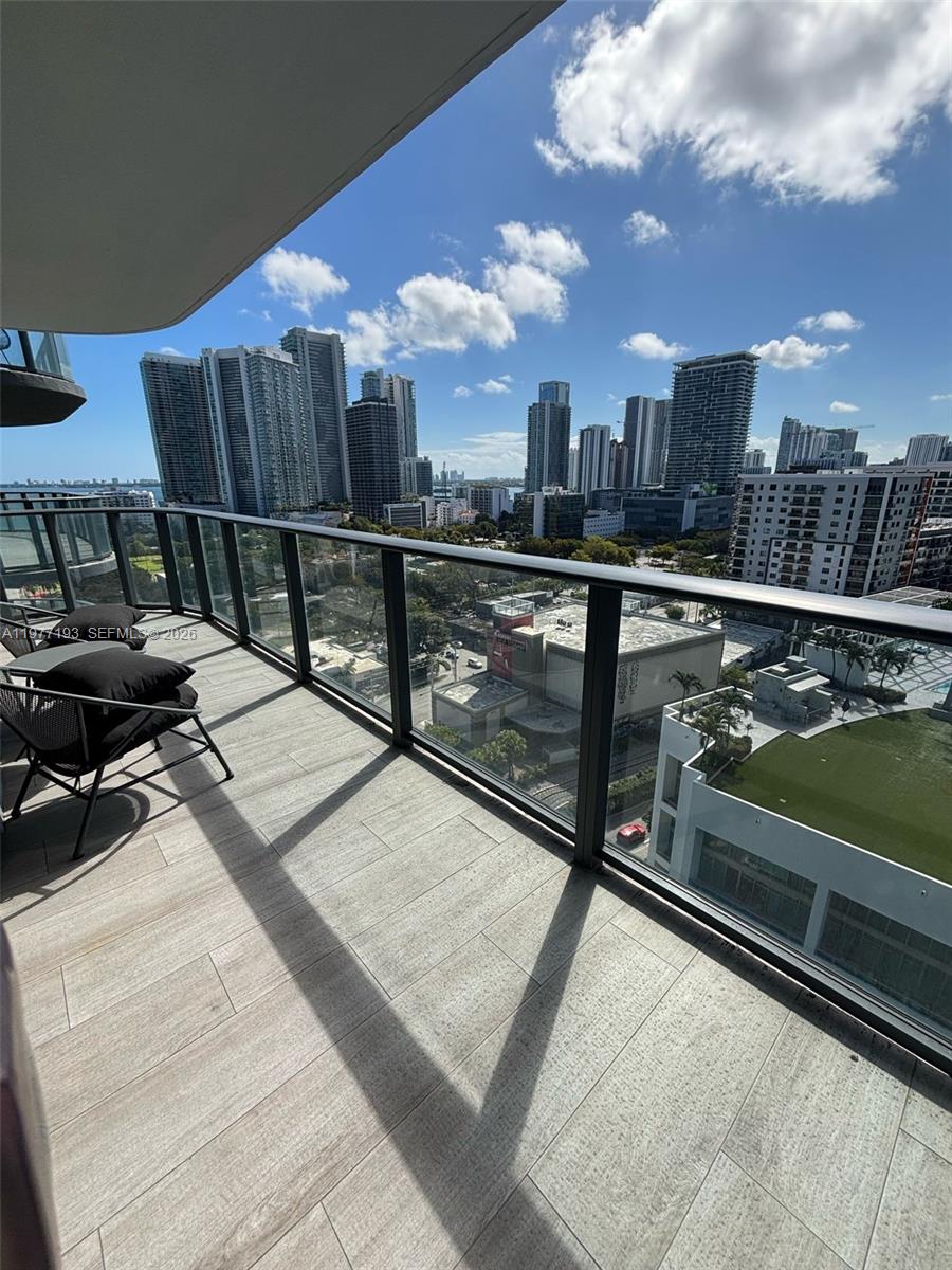 A balcony with tile flooring and glass railings overlooks a city skyline under a blue sky — 121 NE 34th St # 1503, Miami FL 33137, MIAMI, FL