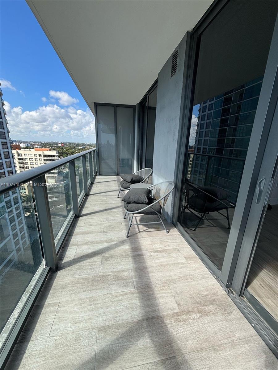 A balcony with tile flooring, two chairs, and a glass railing overlooking a city view — 121 NE 34th St # 1503, Miami FL 33137, MIAMI, FL