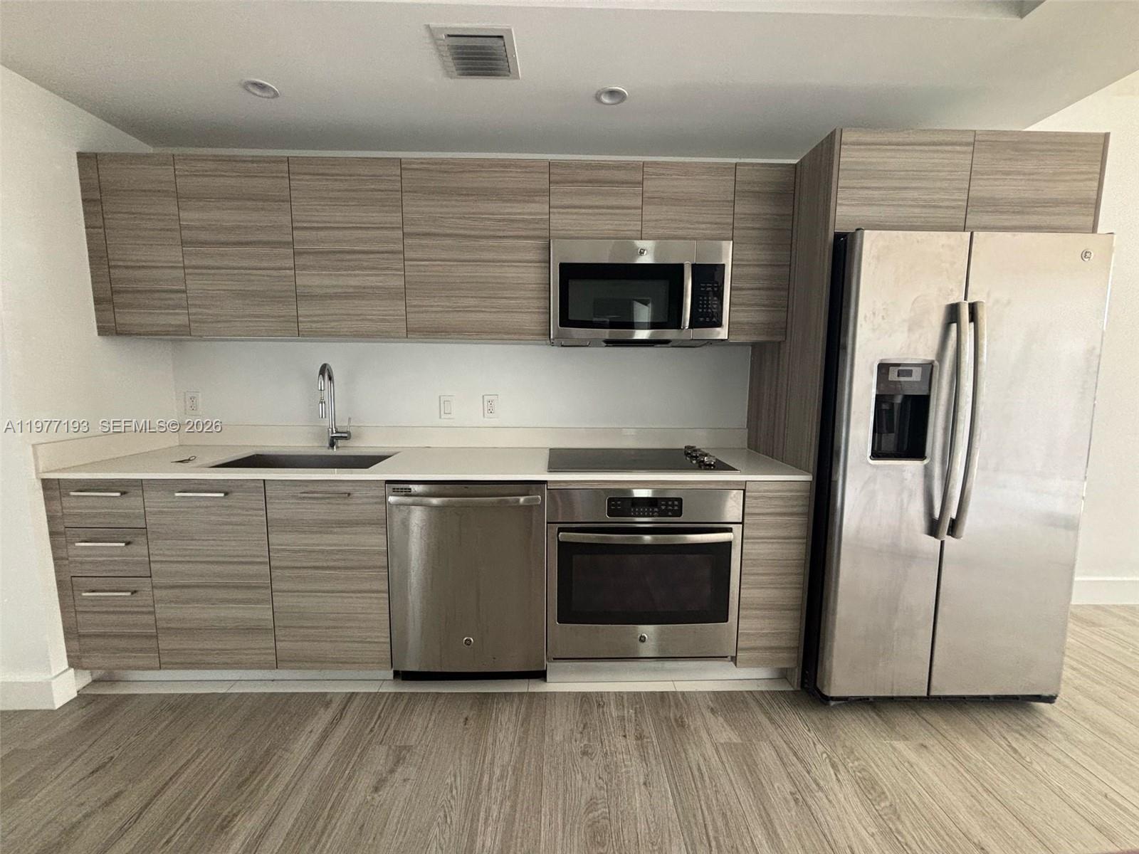 A modern kitchen features wood-grain cabinets, stainless steel appliances, and white countertops — 121 NE 34th St # 1503, Miami FL 33137, MIAMI, FL
