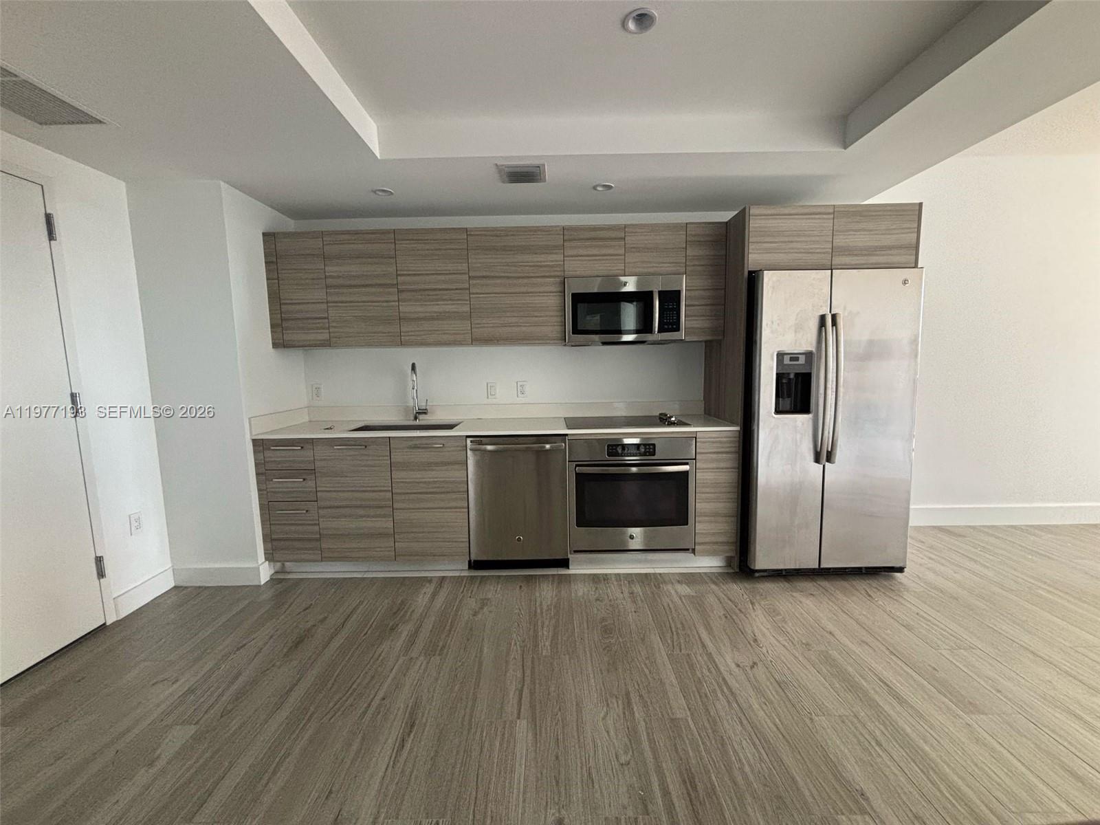 A modern kitchen features wood-grain cabinets, stainless steel appliances, and light-colored countertops — 121 NE 34th St # 1503, Miami FL 33137, MIAMI, FL