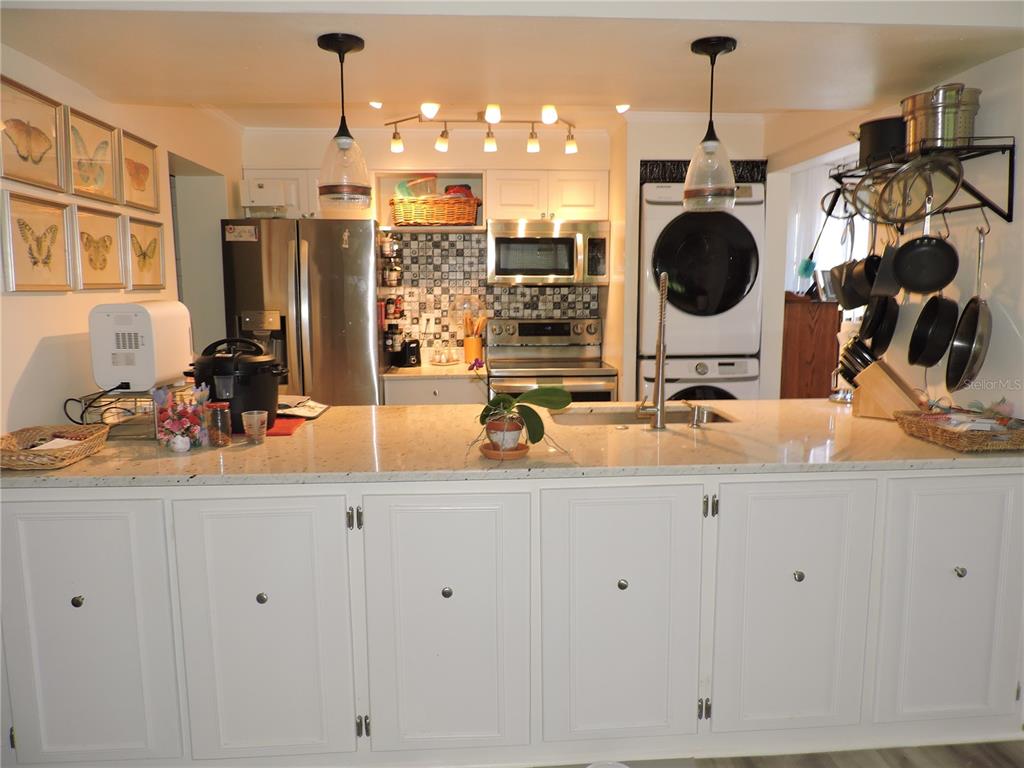 A kitchen features white cabinets, a granite island, stainless steel appliances, and a laundry unit — 118 LA CASA UNIT 118, LAKE WALES, FL