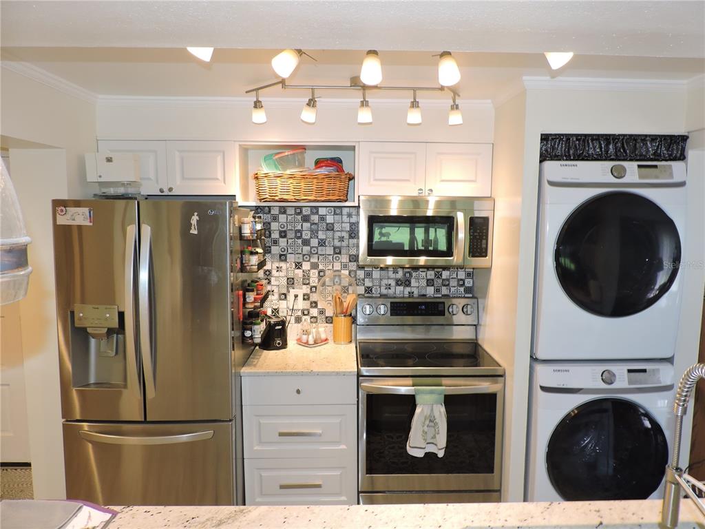 A kitchen features stainless steel appliances, a patterned tile backsplash, and a stacked laundry unit — 118 LA CASA UNIT 118, LAKE WALES, FL