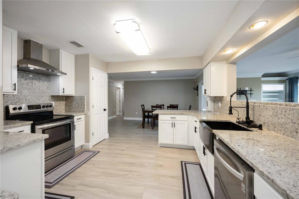 A kitchen features white cabinets, granite countertops, stainless steel appliances, and light wood-look flooring — 4413 MCKIBBEN DRIVE, NORTH PORT, FL