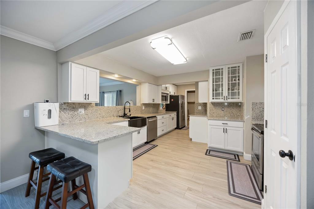 A kitchen features white cabinets, granite countertops, stainless steel appliances, and light wood-look flooring — 4413 MCKIBBEN DRIVE, NORTH PORT, FL