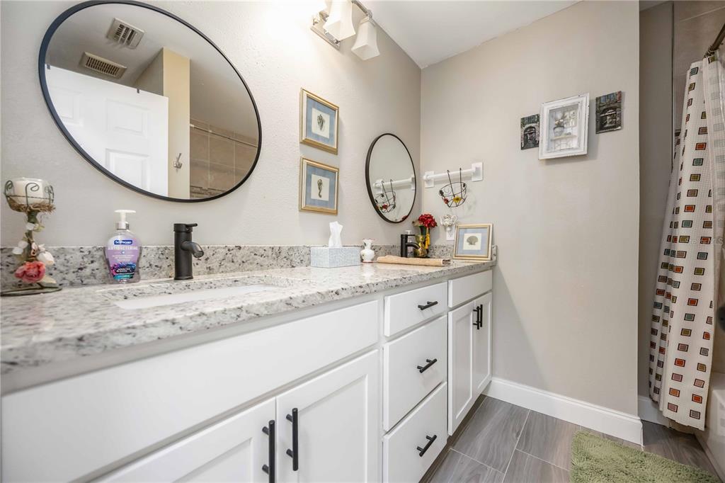 A bathroom features a double vanity with white cabinets, granite countertops, and two round mirrors — 4413 MCKIBBEN DRIVE, NORTH PORT, FL
