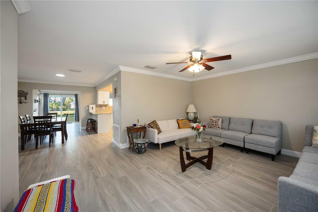 A living room with light wood-look tile floors, a ceiling fan, and an adjacent dining area — 4413 MCKIBBEN DRIVE, NORTH PORT, FL
