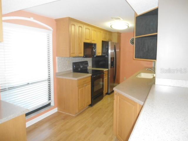 A kitchen features light wood cabinets, stainless steel appliances, and a window with blinds — 2700 COVE CAY DRIVE UNIT 5D, CLEARWATER, FL