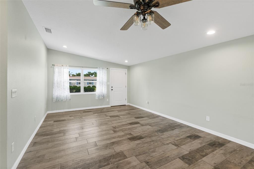 A living room features light green walls, wood-look tile flooring, a ceiling fan, and a door — 143 AVALON AVENUE, FLAGLER BEACH, FL