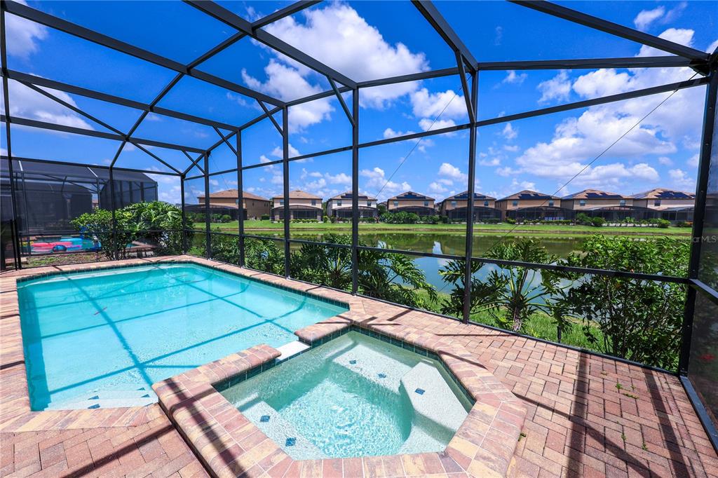 A screened-in pool and spa overlook a lake behind a row of suburban houses — 8811 MACAPA DRIVE, KISSIMMEE, FL