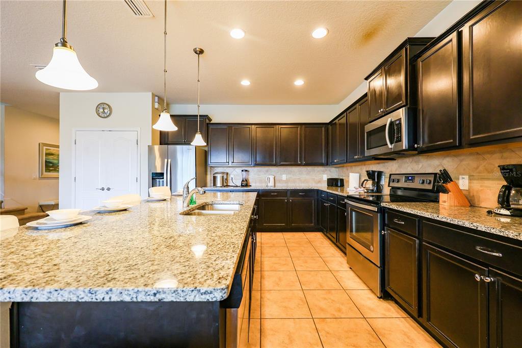 A kitchen features dark wood cabinets, granite countertops, a large island, and stainless steel appliances — 8811 MACAPA DRIVE, KISSIMMEE, FL