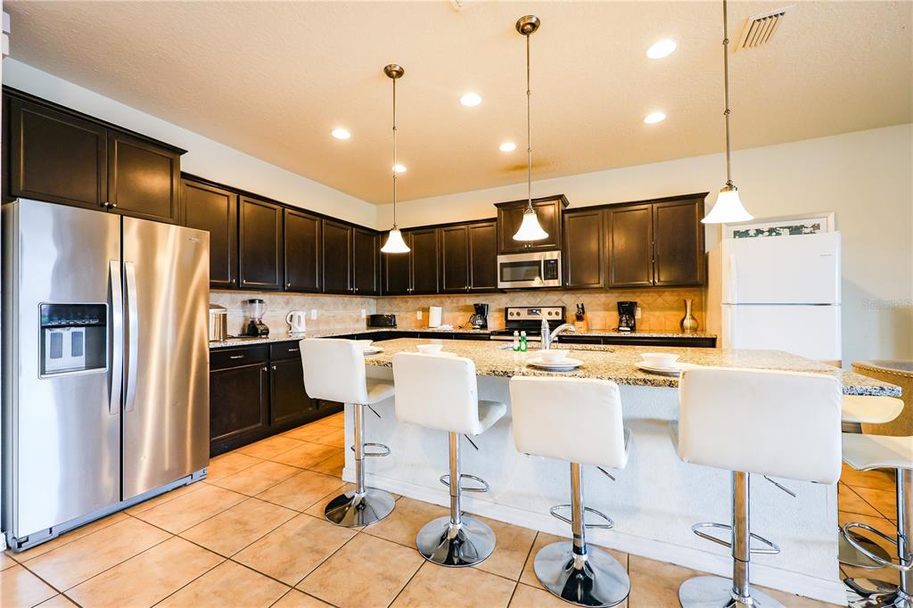 A kitchen features dark cabinetry, granite countertops, a large island with bar stools, and tile flooring — 8811 MACAPA DRIVE, KISSIMMEE, FL