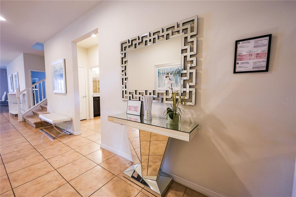 A tiled entryway features a mirrored console table, a geometric wall mirror, and a staircase — 8811 MACAPA DRIVE, KISSIMMEE, FL