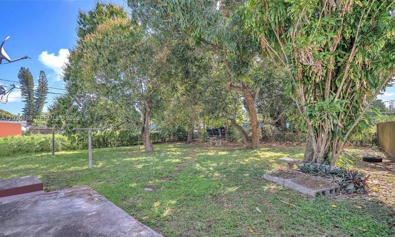 A grassy backyard features several mature trees, a clothesline, and a concrete patio area — 1236 Jann Ave, Opa-Locka FL 33054, OPA-LOCKA, FL