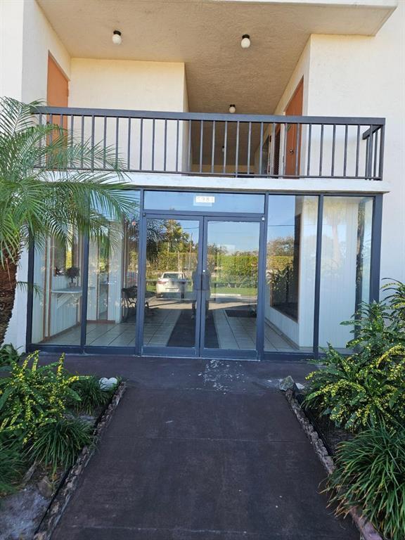 A glass-enclosed entryway leads to a building with a second-story balcony and metal railing — 5981 Via Vermilya # 203, Lake Worth FL 33462, LAKE WORTH, FL