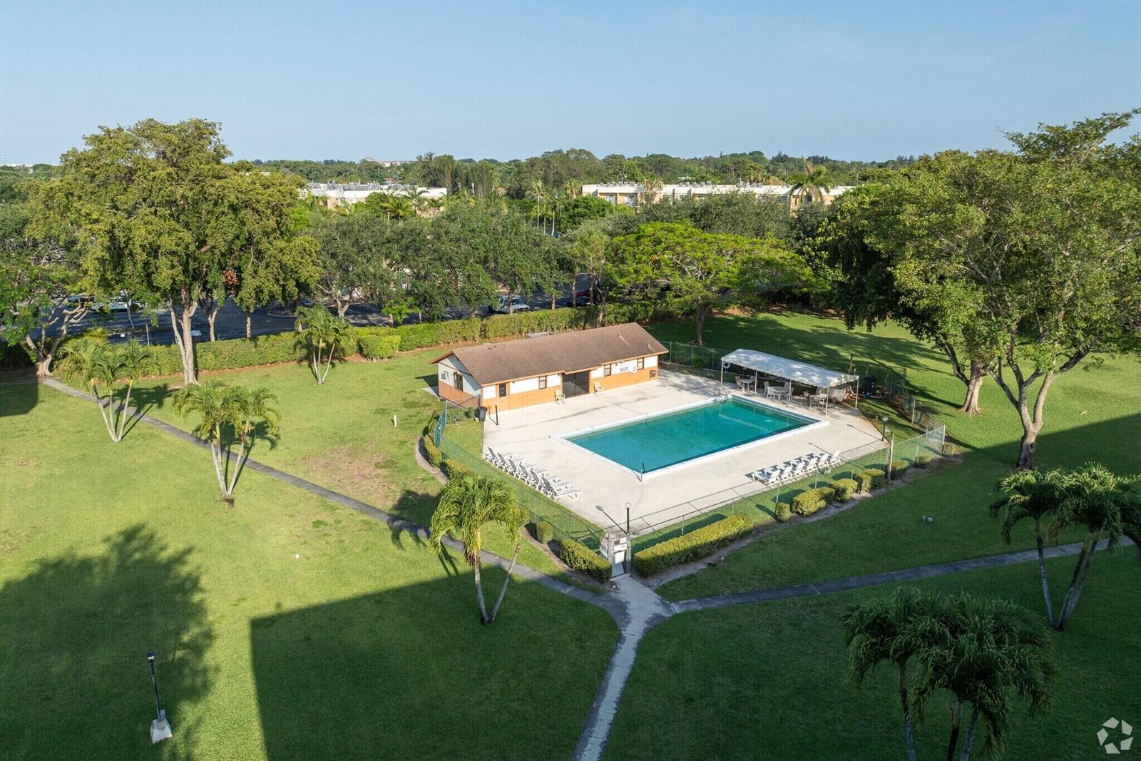 An aerial view of a swimming pool area with a clubhouse, patio, and surrounding lawn — 5981 Via Vermilya # 203, Lake Worth FL 33462, LAKE WORTH, FL