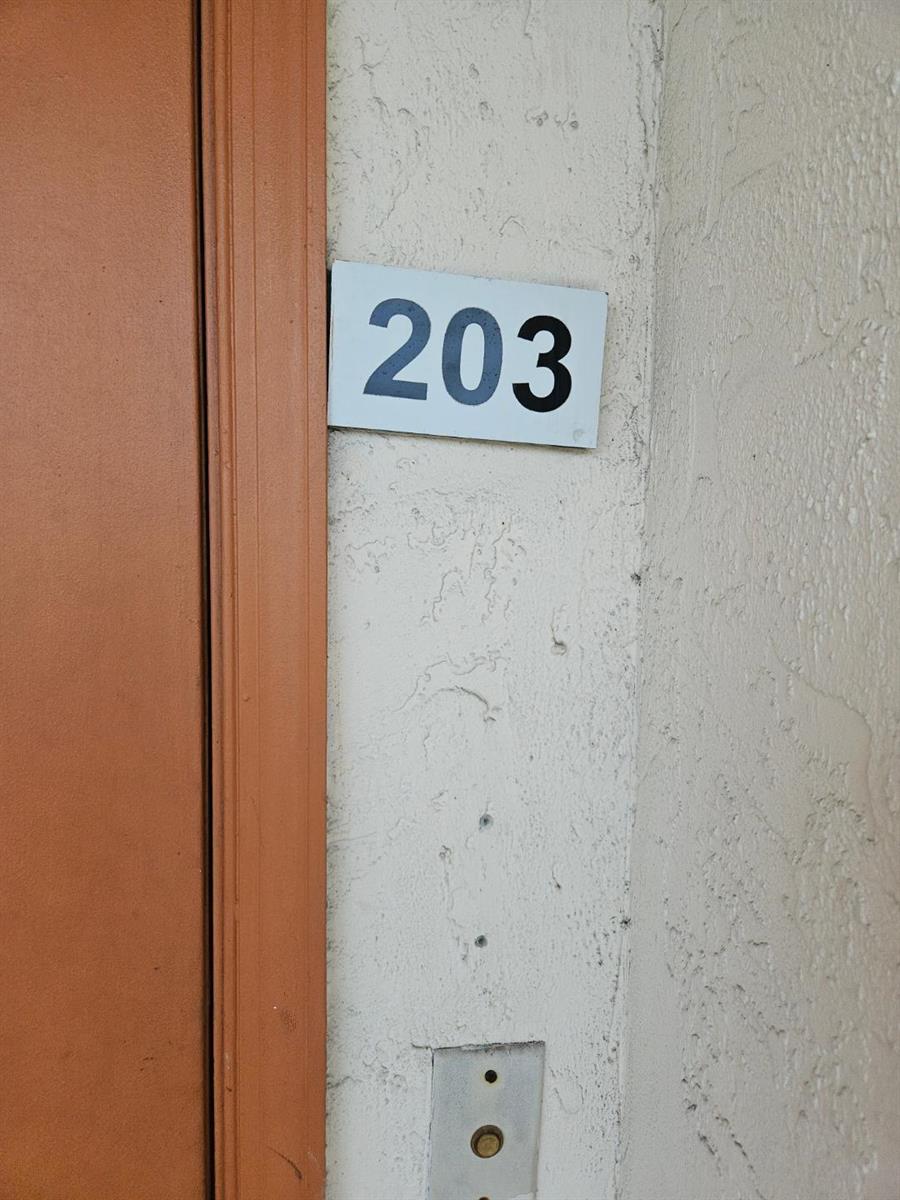 A close-up view shows a white sign with the number 203 mounted on a textured wall — 5981 Via Vermilya # 203, Lake Worth FL 33462, LAKE WORTH, FL