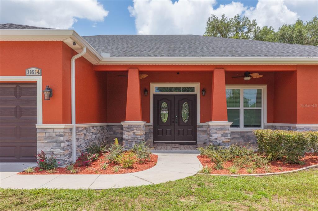 The exterior of a house features orange stucco walls, stone veneer, and a double front door — 39534 SUNBURST DRIVE, DADE CITY, FL