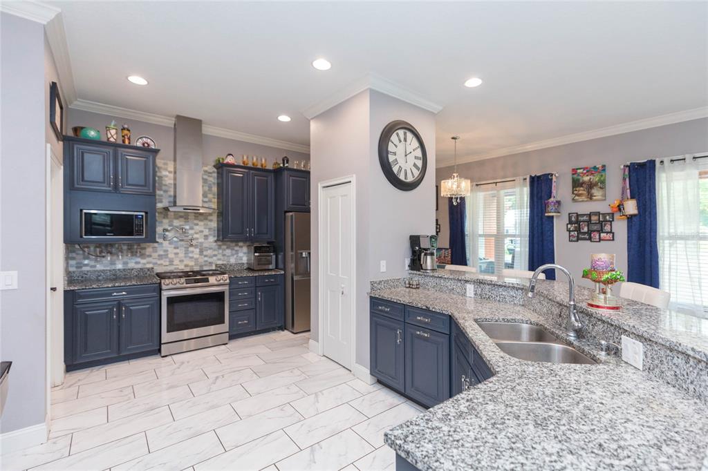 A kitchen features blue cabinets, granite countertops, stainless steel appliances, and white tiled floors — 39534 SUNBURST DRIVE, DADE CITY, FL