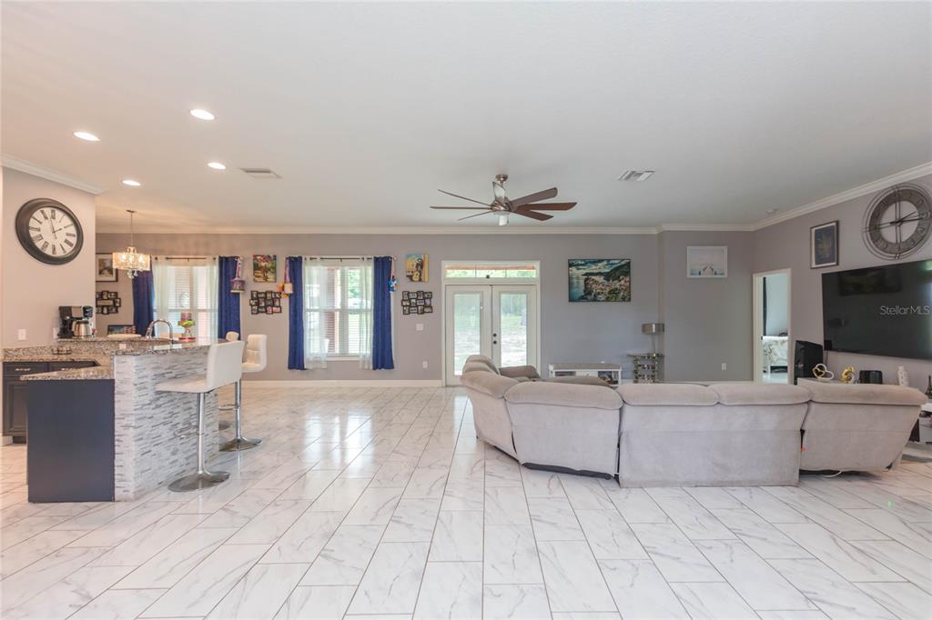 An open-concept living room and kitchen featuring white marble-look tile floors and a sectional sofa — 39534 SUNBURST DRIVE, DADE CITY, FL