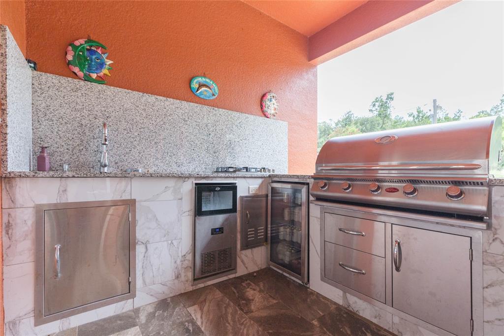 An outdoor kitchen features a stainless steel grill, beverage cooler, ice maker, and granite countertops — 39534 SUNBURST DRIVE, DADE CITY, FL