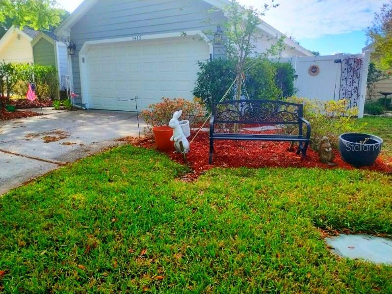 A black metal bench sits on red mulch in front of a house with a garage — 1412 WALDEN OAKS PLACE, PLANT CITY, FL