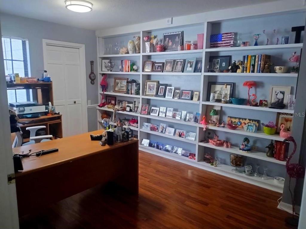 A home office features a wooden desk, hardwood floors, and extensive built-in white shelving — 1412 WALDEN OAKS PLACE, PLANT CITY, FL