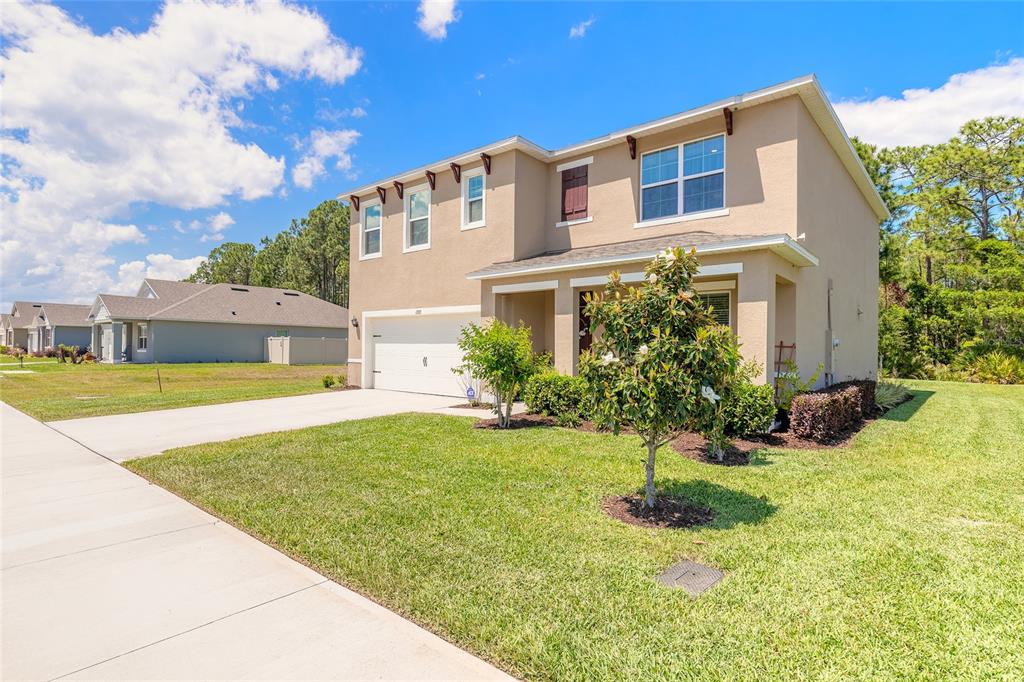 A two-story suburban house with a tan stucco exterior, a garage, and a front lawn — 1333 MORNING WALK DRIVE, ORMOND BEACH, FL
