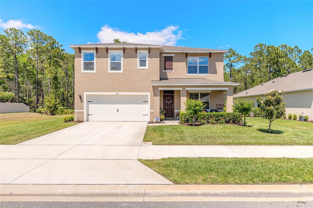 A two-story suburban house with a tan stucco exterior, a two-car garage, and a front porch — 1333 MORNING WALK DRIVE, ORMOND BEACH, FL