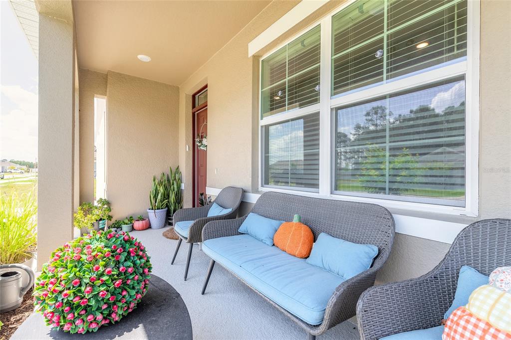 A covered front porch features gray wicker furniture with blue cushions and seasonal decor — 1333 MORNING WALK DRIVE, ORMOND BEACH, FL