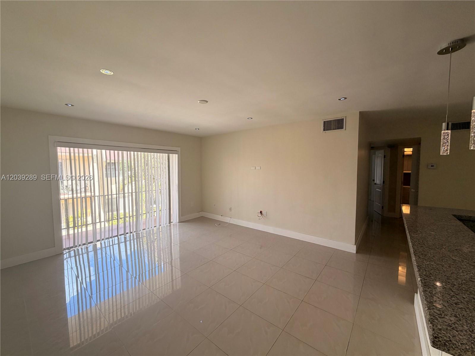 An empty living room features large tile flooring, recessed lighting, and a sliding glass door — 13872 SW 90th Ave, Miami FL 33176, MIAMI, FL