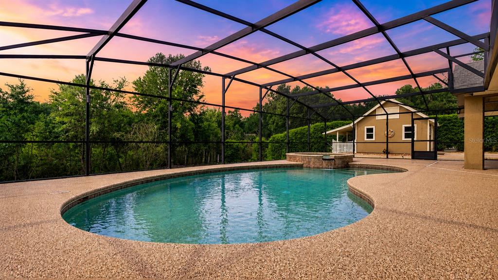 A swimming pool with an attached spa sits inside a screened-in lanai at sunset — 10502 LAKE HILL DRIVE, CLERMONT, FL
