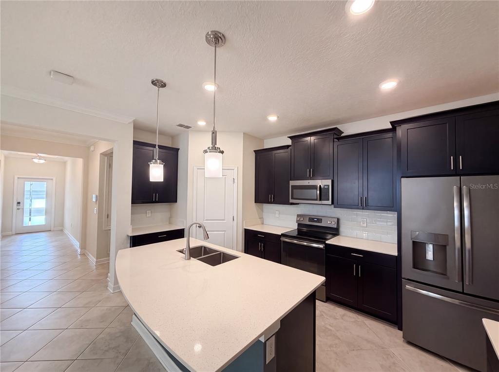 A kitchen features dark cabinets, a large white island with a sink, and stainless appliances — 4112 INNOVATION LANE, CLERMONT, FL