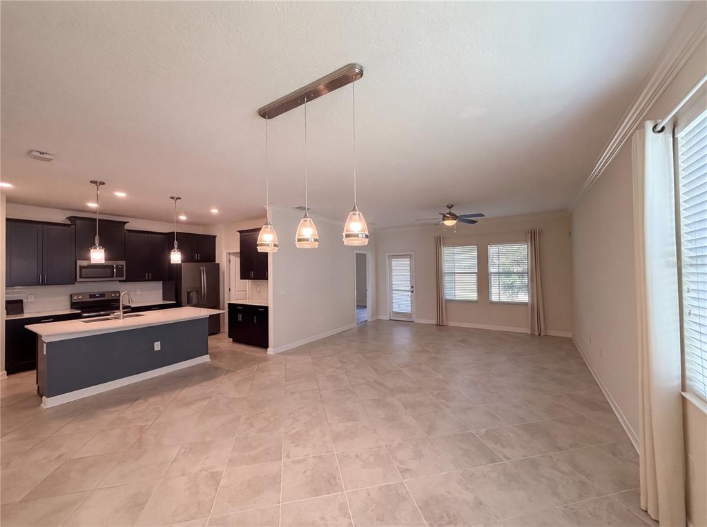 An open-concept kitchen with dark cabinets and an island overlooks a spacious tiled living area — 4112 INNOVATION LANE, CLERMONT, FL