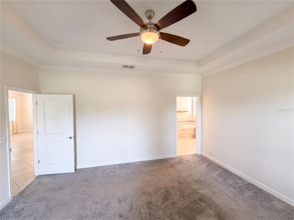 A bedroom with gray carpet, a tray ceiling with a fan, and two doorways — 4112 INNOVATION LANE, CLERMONT, FL