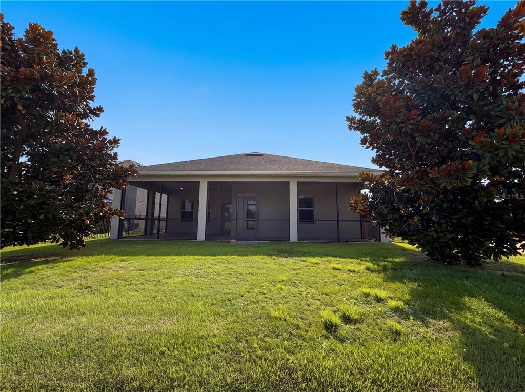 A rear view of a house with a screened-in porch and large trees on both sides — 4112 INNOVATION LANE, CLERMONT, FL