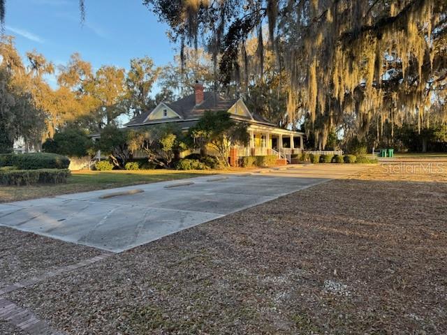A yellow house with a wraparound porch sits behind a large concrete parking area — 11294 N US HIGHWAY 301, OXFORD, FL