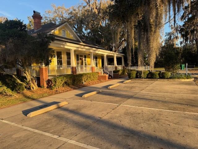 A yellow house with a brick chimney and a large front porch sits beside a parking lot — 11294 N US HIGHWAY 301, OXFORD, FL