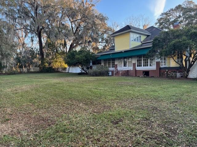 A two-story yellow house with a green awning sits behind a large grassy yard — 11294 N US HIGHWAY 301, OXFORD, FL