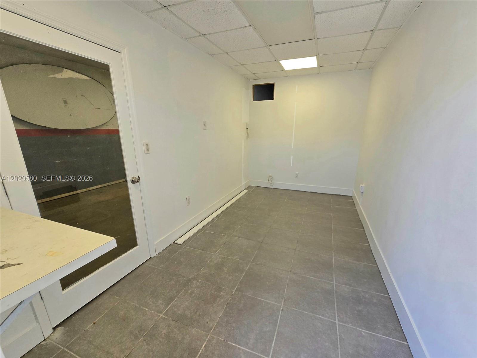 A small, empty room features white walls, gray tile flooring, and a glass-paneled door — 7909 NW 64th St # 7909, Medley FL 33166, MEDLEY, FL