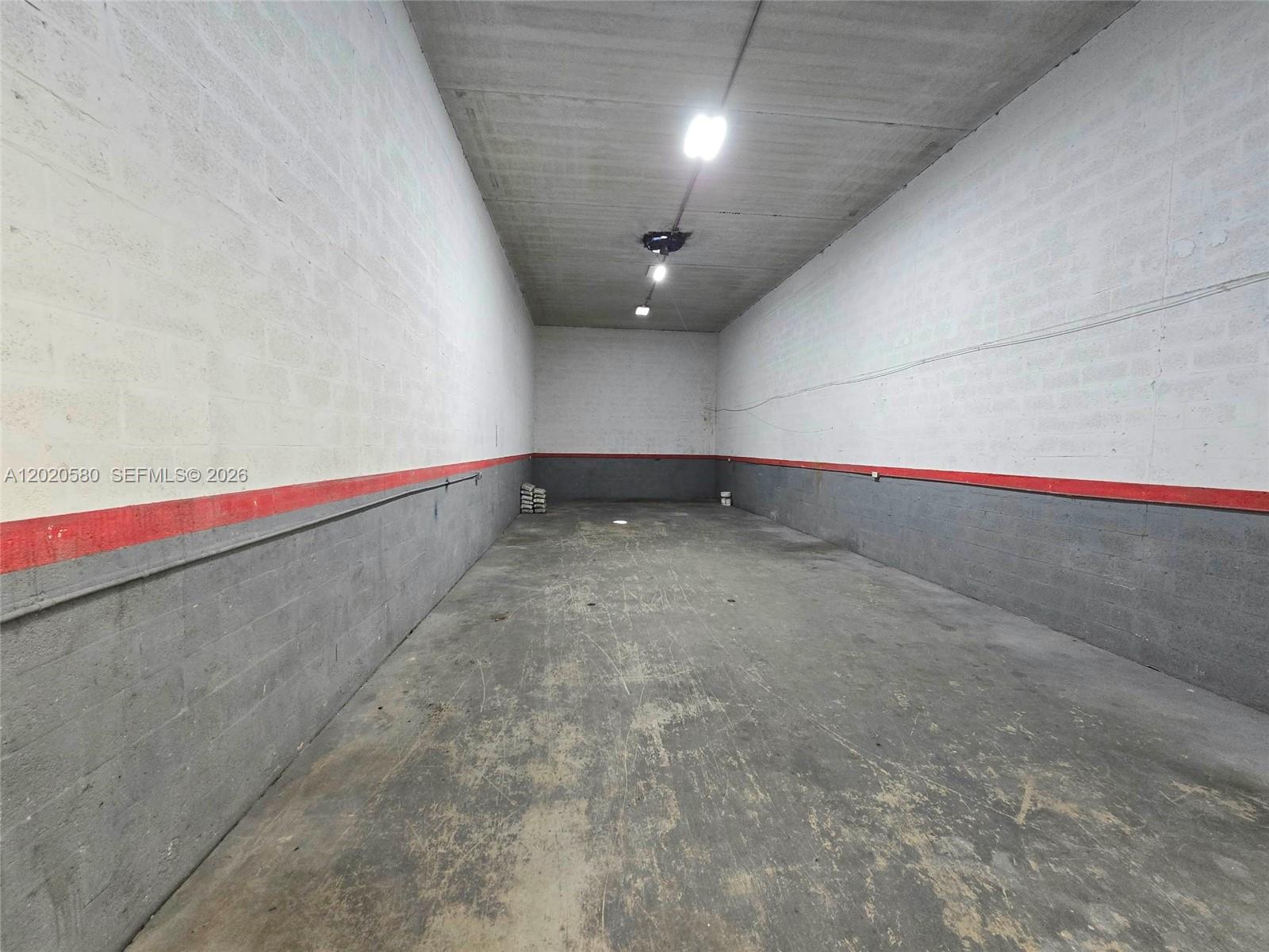 An empty industrial storage unit features concrete block walls, a concrete floor, and overhead lighting — 7909 NW 64th St # 7909, Medley FL 33166, MEDLEY, FL