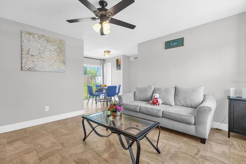 A living room with tile floors, a gray sofa, a glass coffee table, and ceiling fan — 5390 BOTANY COURT, ORLANDO, FL