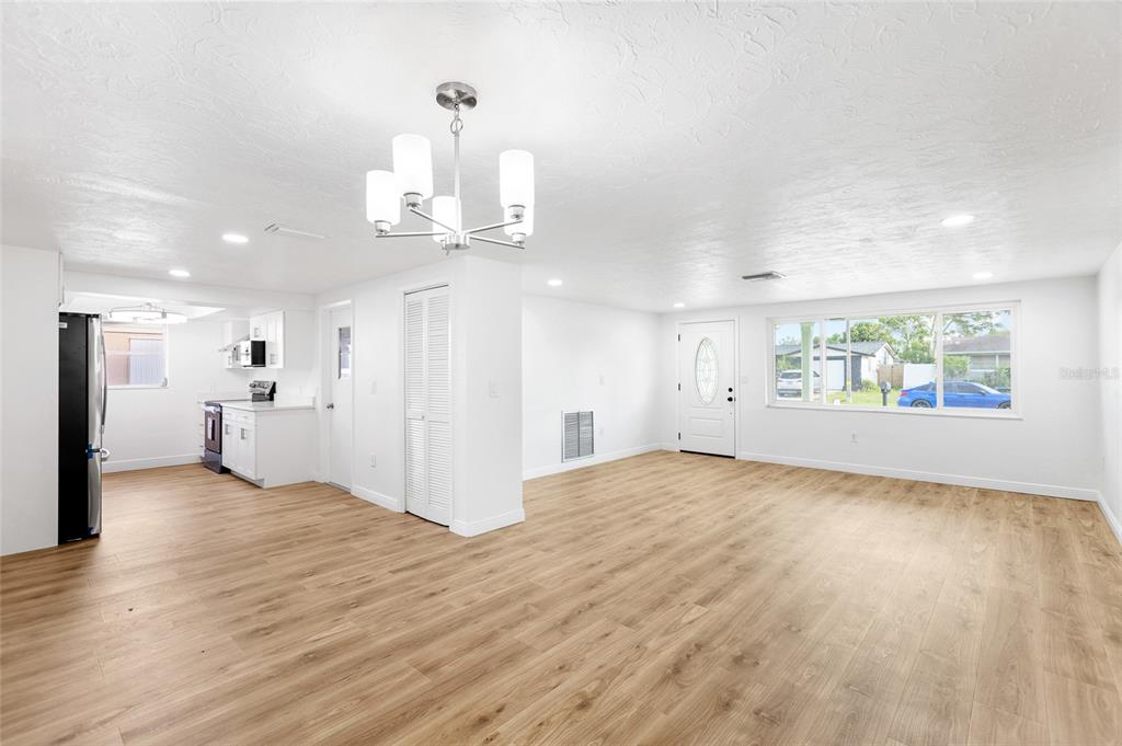 An open-concept living area with light wood-look flooring, white walls, and an adjacent kitchen — 6239 7TH AVENUE, NEW PORT RICHEY, FL